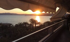 Ein Sonnenuntergangsblick von einem Balkon mit Geländer, Palmen und einer entfernten Brücke.
