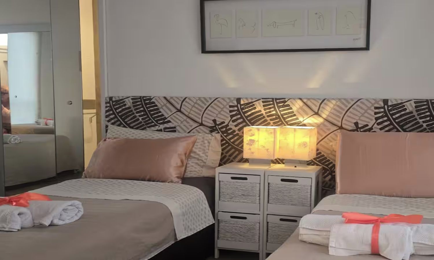 Habitación de hotel con dos camas, una mesita de noche con lámpara y un cuadro en la pared.