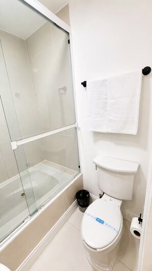 A bathroom with a toilet, a glass-enclosed shower, and a white towel hanging on the wall. - Estudio / StayMty San Agustín. #2 (San Pedro Garza García)