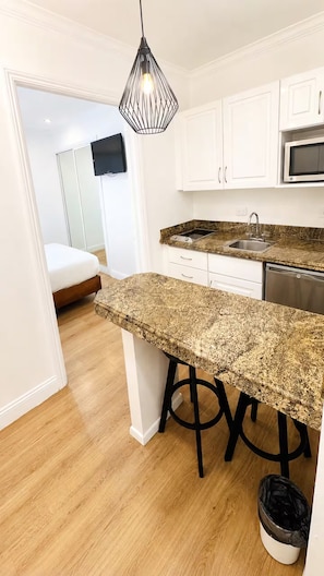 A kitchen with white cabinets, a granite countertop, a stainless steel sink, and a black trash bin.
