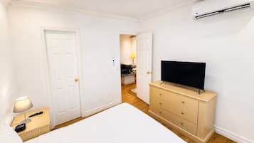 A hotel room with a bed, a dresser, a television, and an air conditioning unit.