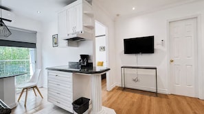 A modern kitchen with white cabinetry, a black countertop, a coffee maker, and a TV mounted on the wall. - Suite 1 Recámara / StayMty San Agustín #3 (San Pedro Garza García)