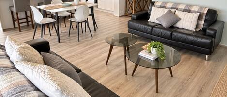 A modern living room with a sofa, a glass coffee table, and a dining area with chairs and a table.