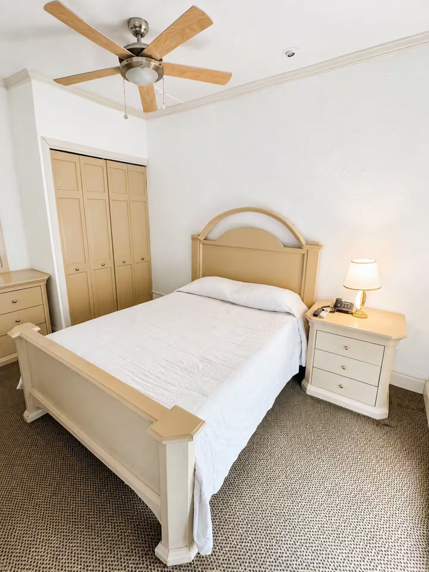 Ein Schlafzimmer mit einem Bett, einem Nachttisch, einer Lampe, einem Deckenventilator und einem Kleiderschrank.