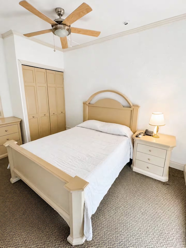 A bedroom with a bed, a nightstand, a lamp, a ceiling fan, and a wardrobe.