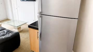 Eine moderne Küche mit einem Edelstahlkühlschrank, einem Esstisch mit Glasplatte und einem wandmontierten Flachbildfernseher.