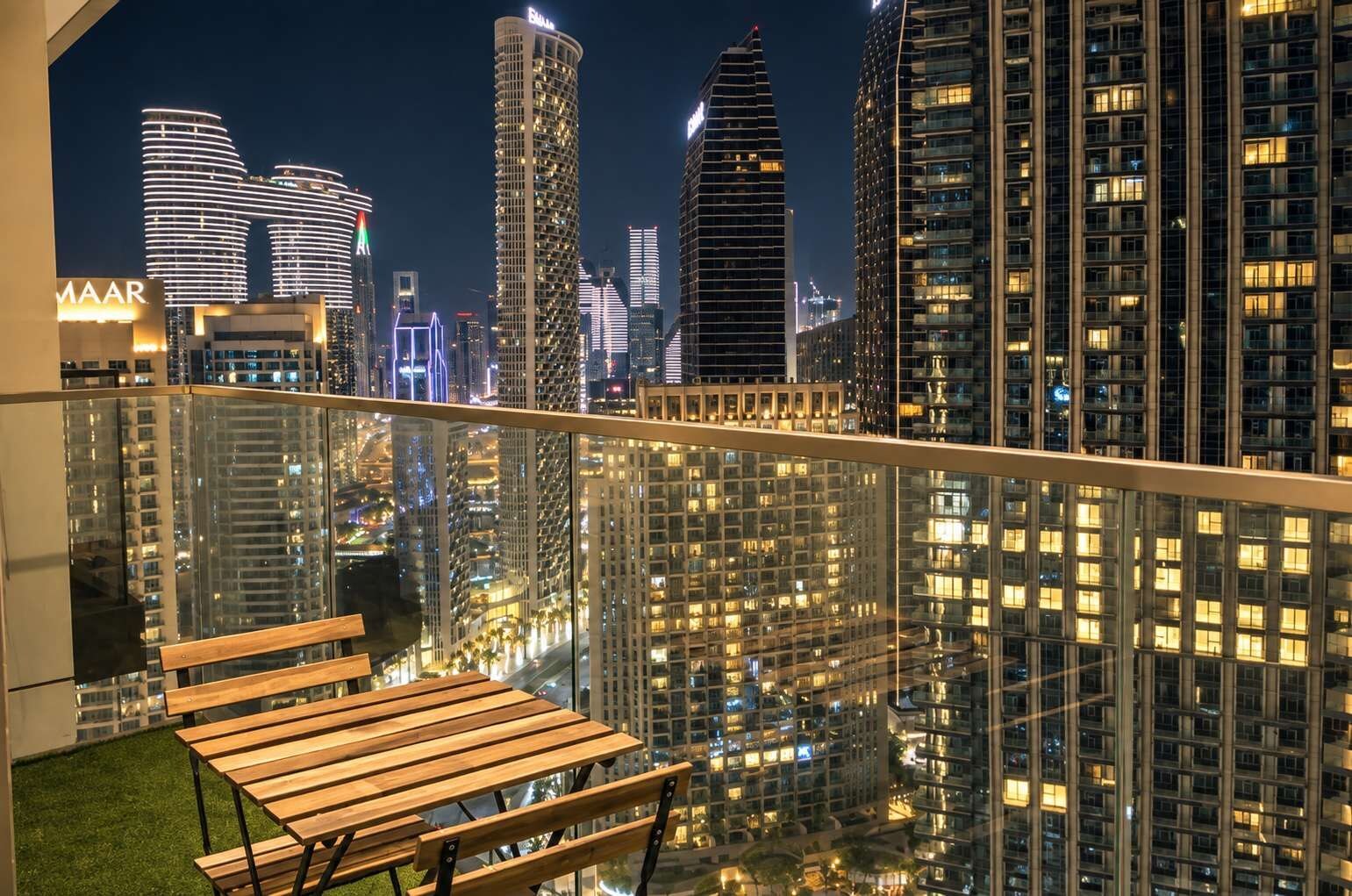 A balcony with a wooden bench overlooking a cityscape at night.