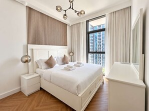 Habitación de hotel con una cama grande, mesitas de noche, armario, candelabro moderno y un gran ventanal con cortinas.