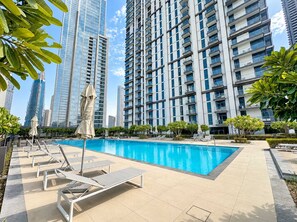 A swimming pool with lounge chairs and umbrellas, surrounded by high-rise buildings. - Luxury 1BR Downtown Views Walk to Burj Khalifa (Dubai)