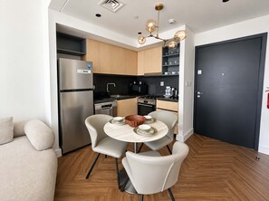 Een kleine keuken met moderne apparatuur, een eethoek met een ronde tafel en stoelen, en een donkere deur.