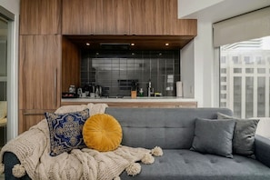 A modern living room with a grey sofa, a knitted throw blanket, and decorative pillows. - Chic 1 BR Yorkville  Suite (Toronto)