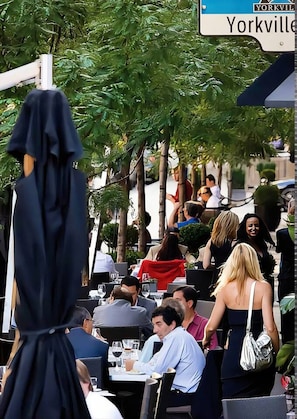 An outdoor dining area with tables and chairs, surrounded by trees and a street sign. - Chic 1 BR Yorkville  Suite (Toronto)