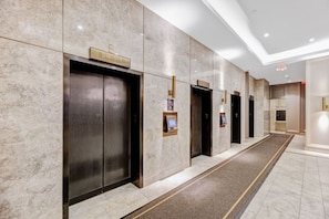 Un couloir d’hôtel aux murs de marbre, doté de plusieurs ascenseurs, chacun étant muni d’une indication du numéro de l’étage.