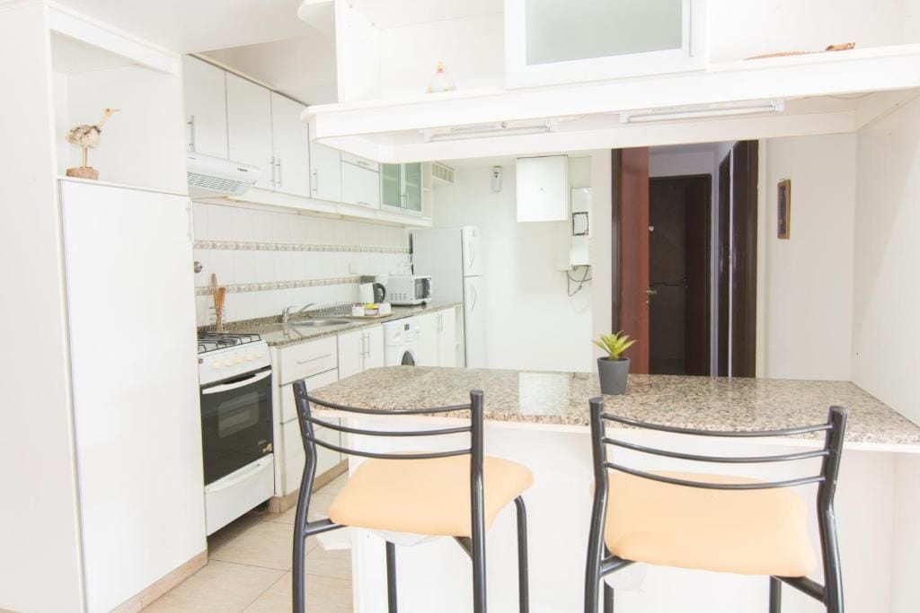 A kitchen with white cabinets, a stove, a microwave, and two bar stools.