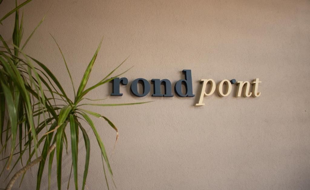 En vägg med texten ”rond pont” skriven med en stiliserad typsnitt, och en växt till vänster.