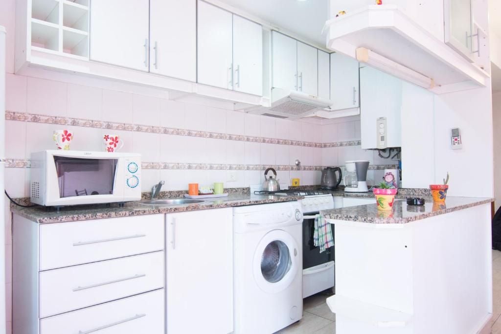 Una cocina con armarios blancos, microondas, lavadora y cafetera.
