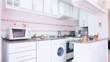 Una cocina con armarios blancos, microondas, lavadora y cafetera.