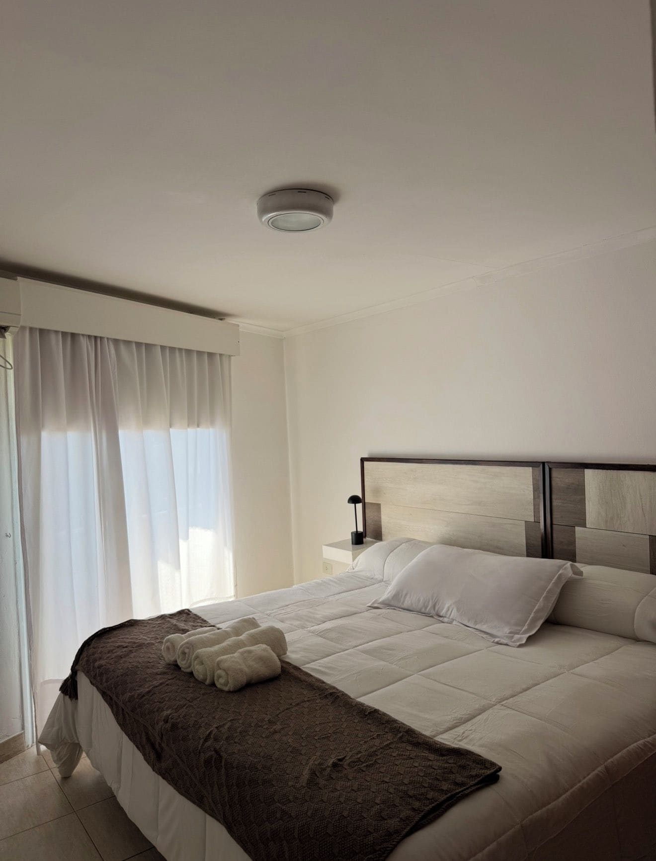Une chambre d’hôtel avec un lit, une table de chevet, une lampe et une fenêtre avec des rideaux.