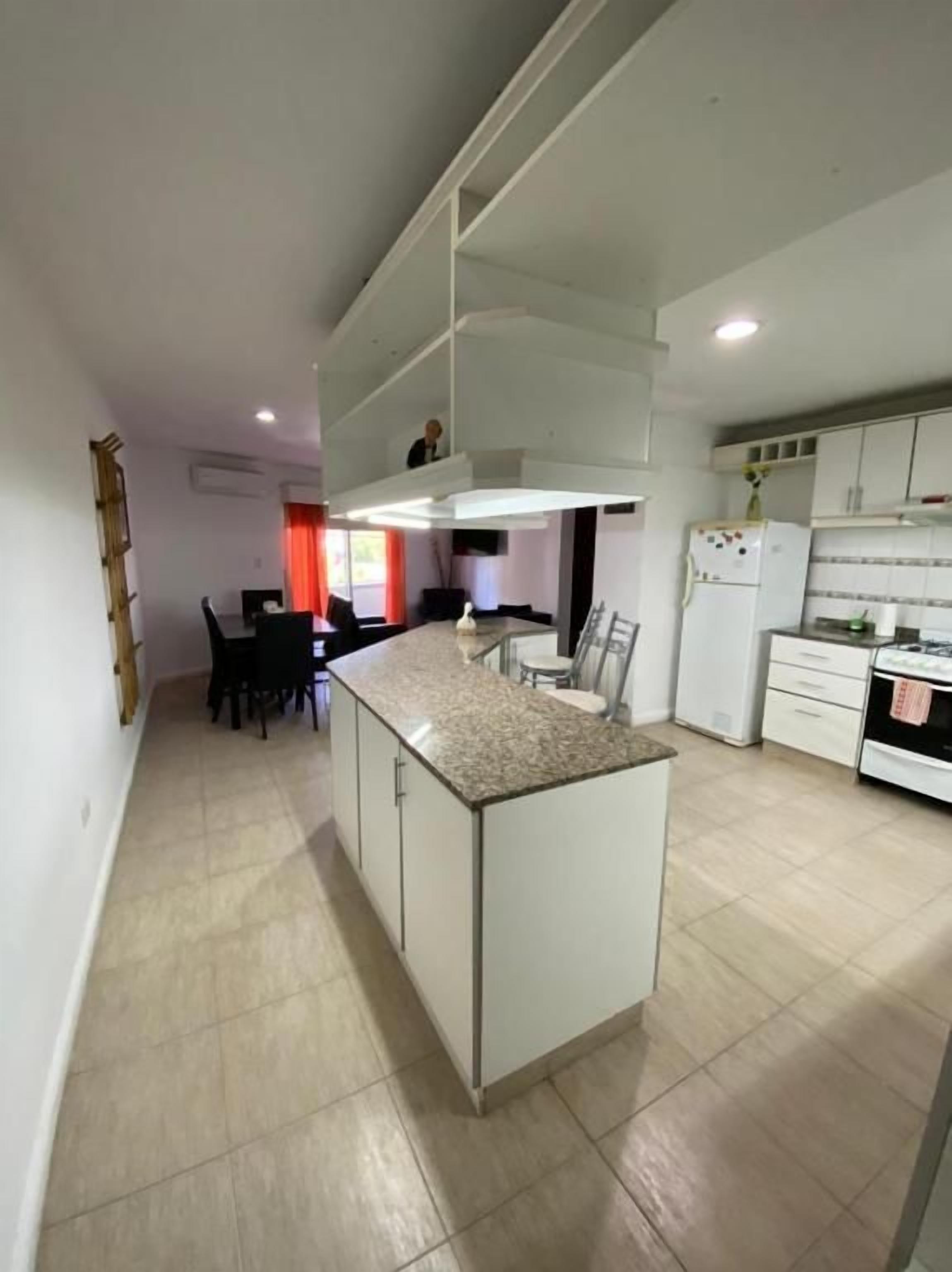 Una cocina moderna con una isla central, armarios blancos y un comedor con sillas.