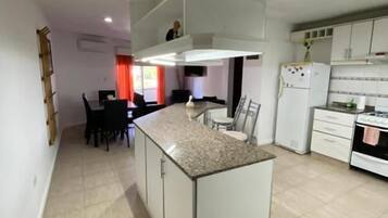 Una cocina moderna con una isla central, armarios blancos y un comedor con sillas.