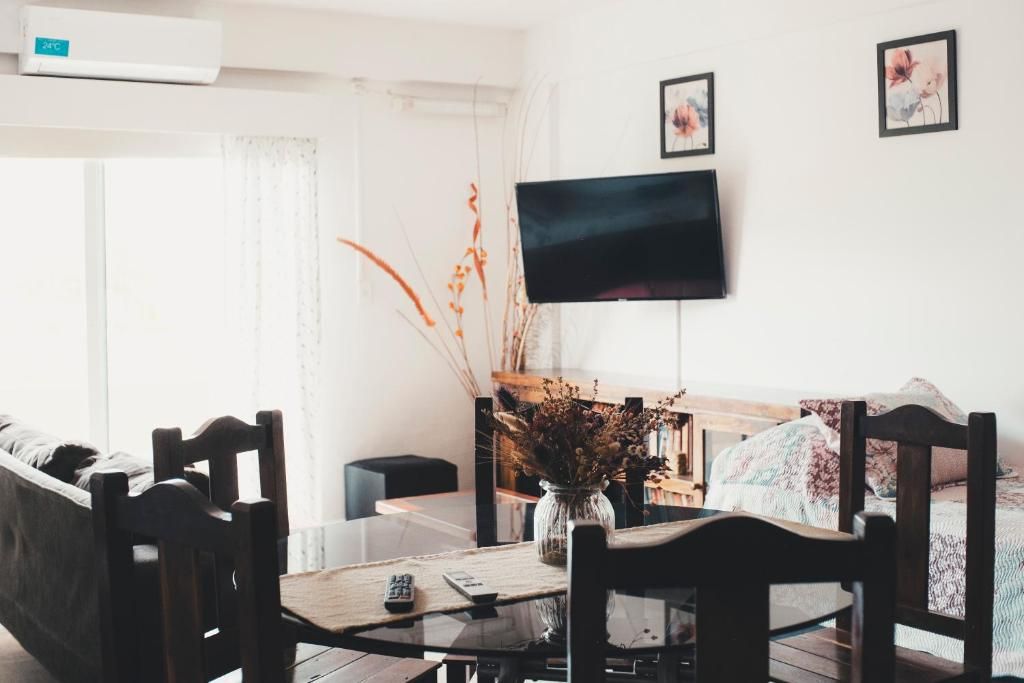 Una sala de estar moderna con una mesa de centro de vidrio, sillas de madera, un televisor de pantalla plana montado en la pared y un sofá con una manta estampada.