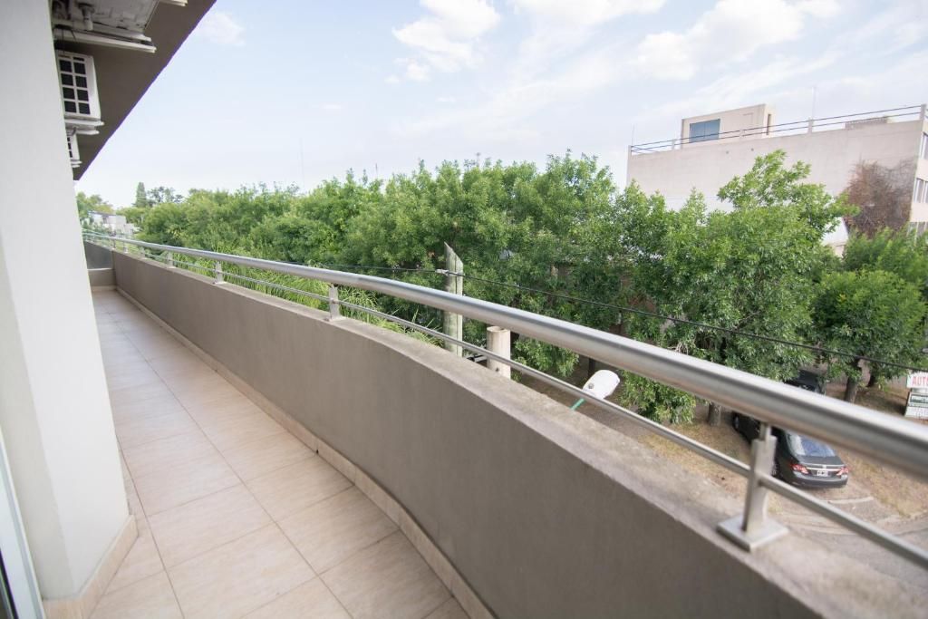A balcony with a metal railing, a tiled floor, and a view of a tree-lined street.