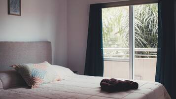 Un dormitorio con cama, almohadas, una ventana y vistas al verde exterior.