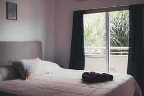 Un dormitorio con cama, almohadas, una ventana y vistas al verde exterior.