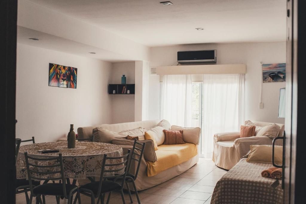 A living room with a sofa, a dining table with chairs, a TV mounted on the wall, and a window with curtains.