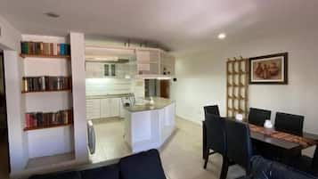 Un salon moderne avec un canapé en cuir noir, un coin repas avec une table et des chaises, et une cuisine en arrière-plan.