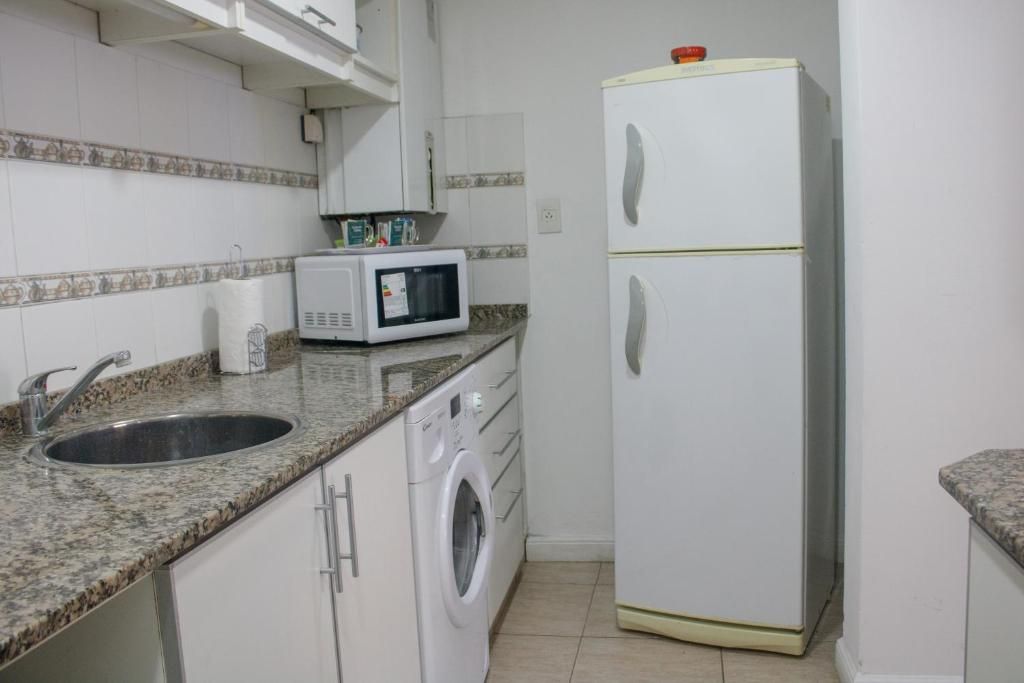 A compact kitchen with a sink, microwave, washing machine, and a double-door refrigerator.
