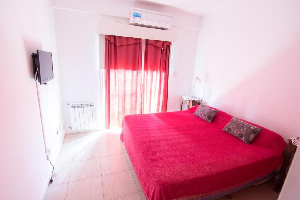 A room with a bed, a television mounted on the wall, and a window with curtains.