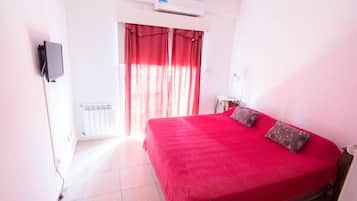 A room with a bed, a television mounted on the wall, and a window with curtains.