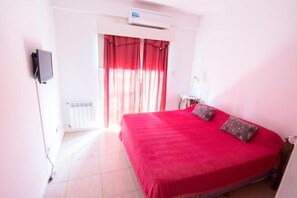Una habitación con una cama, un televisor instalado en la pared y una ventana con cortinas.