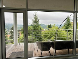 Een balkon met uitzicht op een bergachtig landschap, een hekwerk en rieten meubilair.