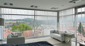 Een moderne slaapkamer met een groot raam, een bank, een nachtkastje en uitzicht op een stadsgezicht.