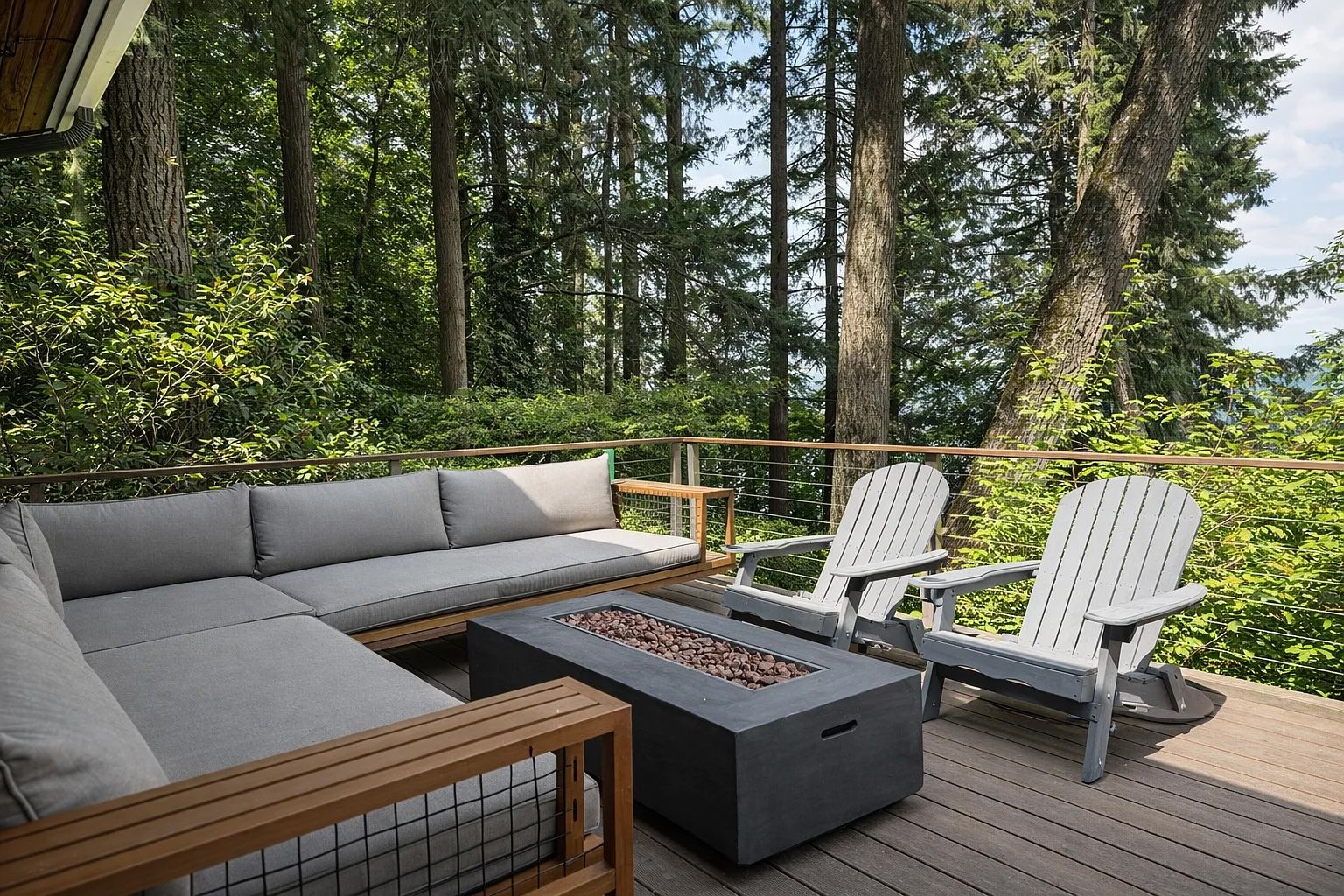 A deck with a sofa, two Adirondack chairs, and a fire pit.