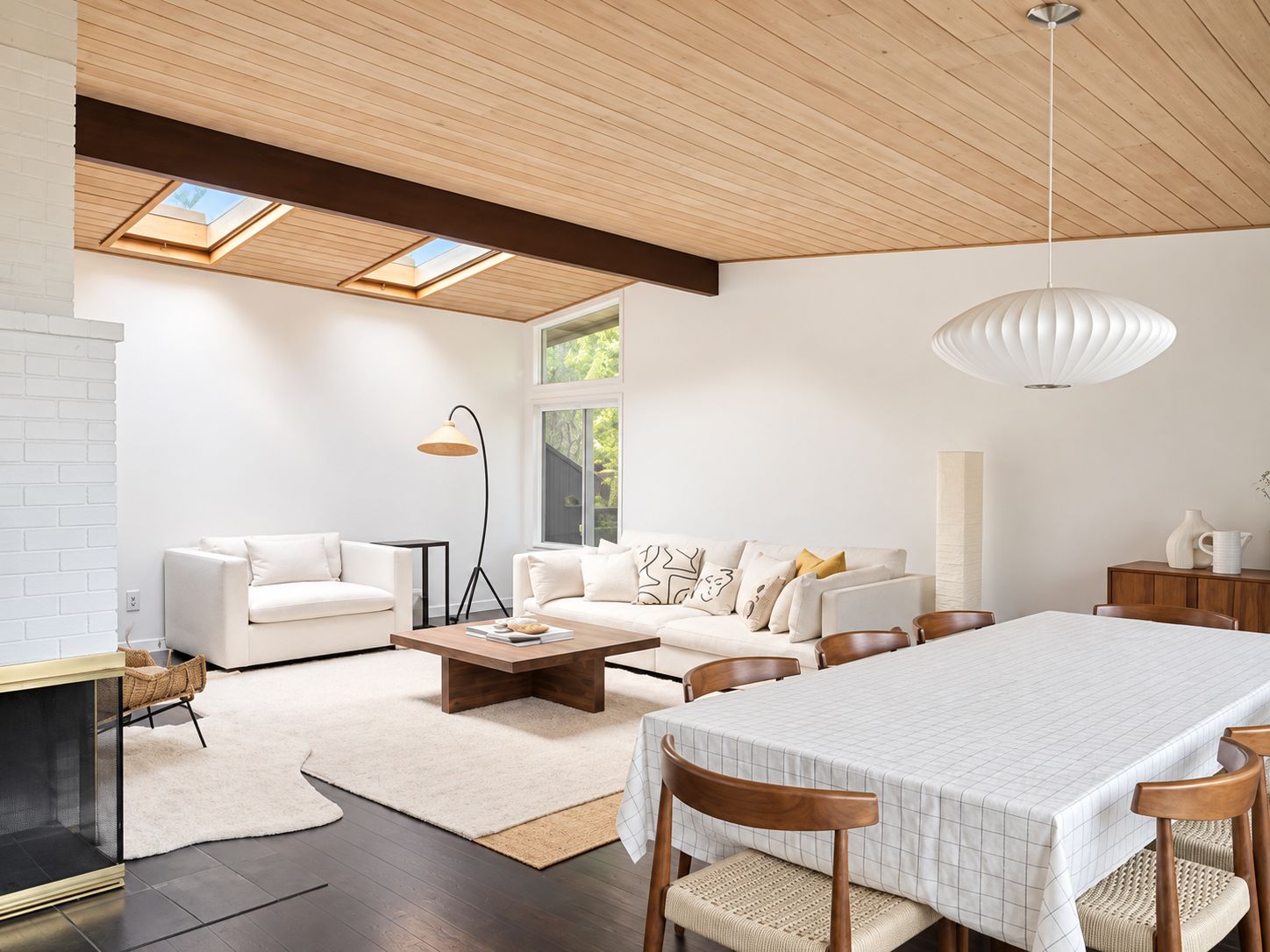 Een moderne woonkamer met een eethoek, met een groot raam, een plafond met dakramen en een witte open haard.