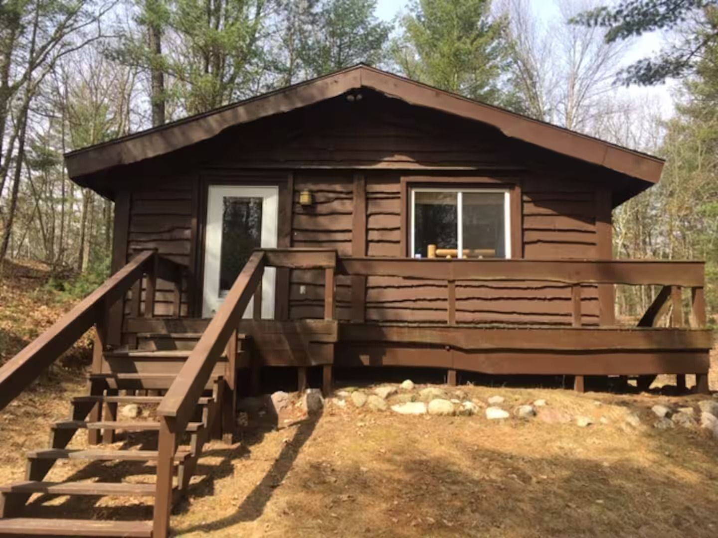 A wooden cabin with a front door, a window, and a staircase leading up to the entrance.