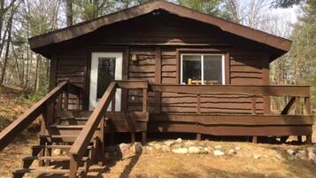 A wooden cabin with a front door, a window, and a staircase leading up to the entrance.