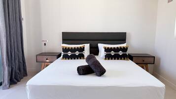 Una habitación de hotel con una cama grande, dos mesitas de noche, un cabecero y una cortina.