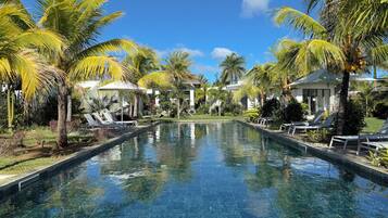 A clear pool with lounge chairs and palm trees, surrounded by buildings.