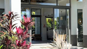 A building entrance with a glass door, a thatched roof, and a small outdoor seating area with a chair.