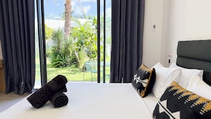 Habitación de hotel con cama, vista a un jardín y una puerta señalizada con 'EXIT'.