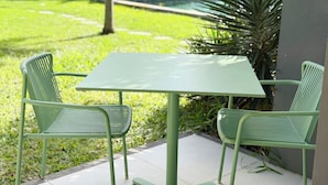 Un patio al aire libre con una mesa y sillas de metal verde, rodeado de follaje y un edificio.