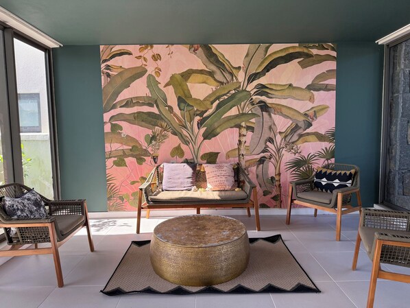 Una habitación con un mural tropical de gran tamaño, un taburete de madera redondo y dos sillas de mimbre.