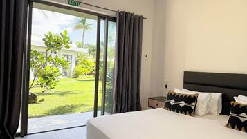 Habitación de hotel con cama, mesita de noche, almohada y vista a un jardín a través de una puerta corredera.