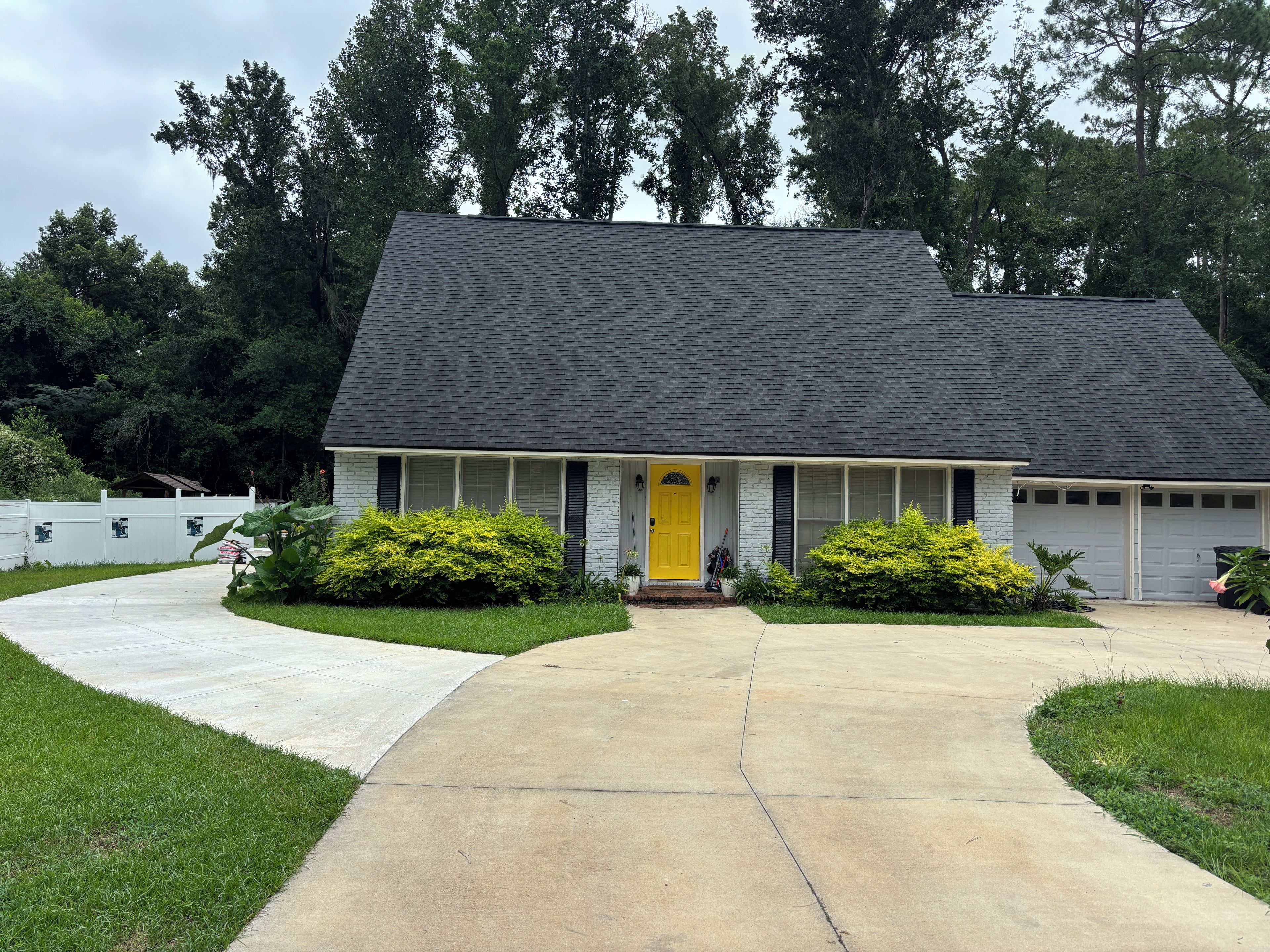 A single-story house with a dark shingled roof, a front porch, and a yellow door.
