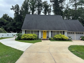 A single-story house with a dark shingled roof, a front porch, and a yellow door.