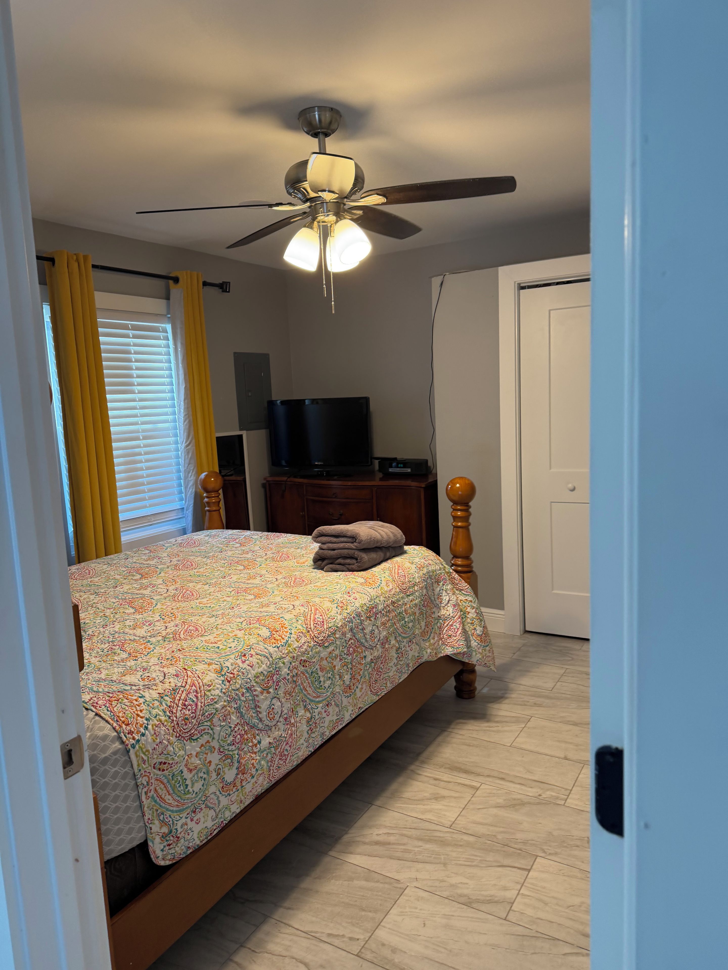 A bedroom with a bed, a ceiling fan, a television, and a door.
